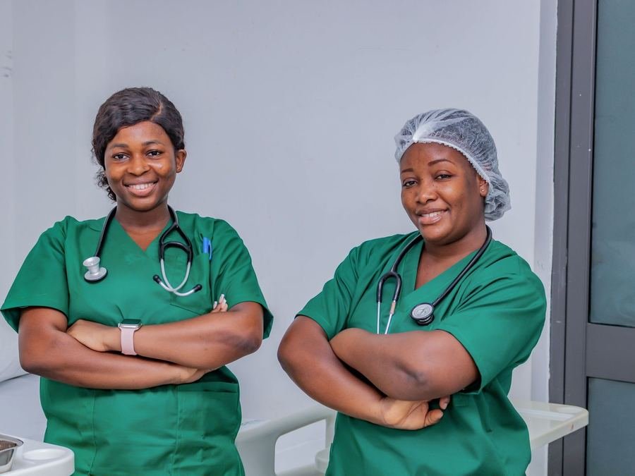 Two smiling healthcare workers in green scrubs with stethoscopes around their necks