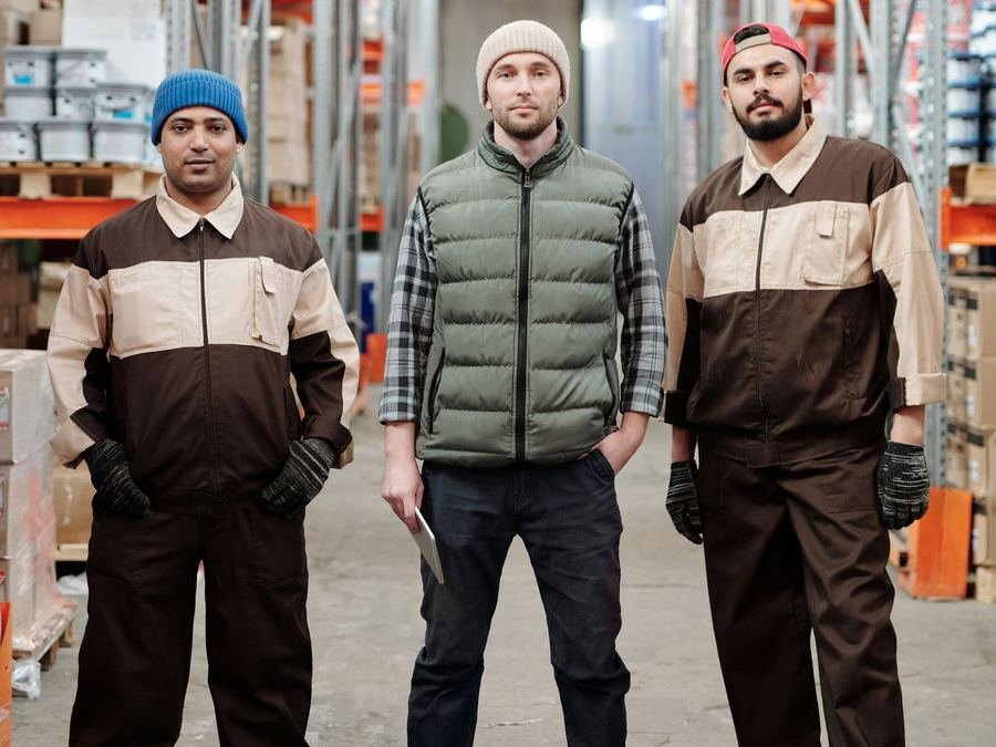 Three warehouse workers in work uniforms standing in front of tall storage racking